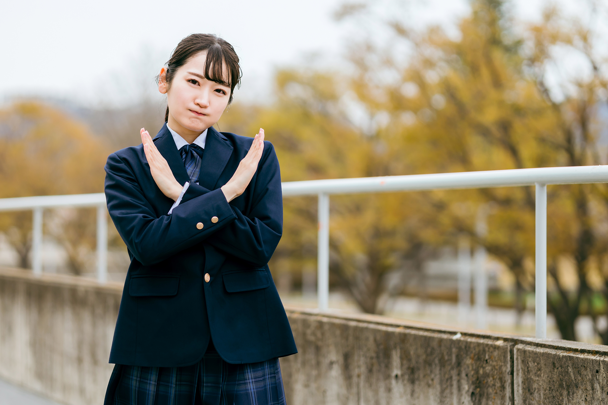 手でバツを作る制服姿の高校生・女子高生