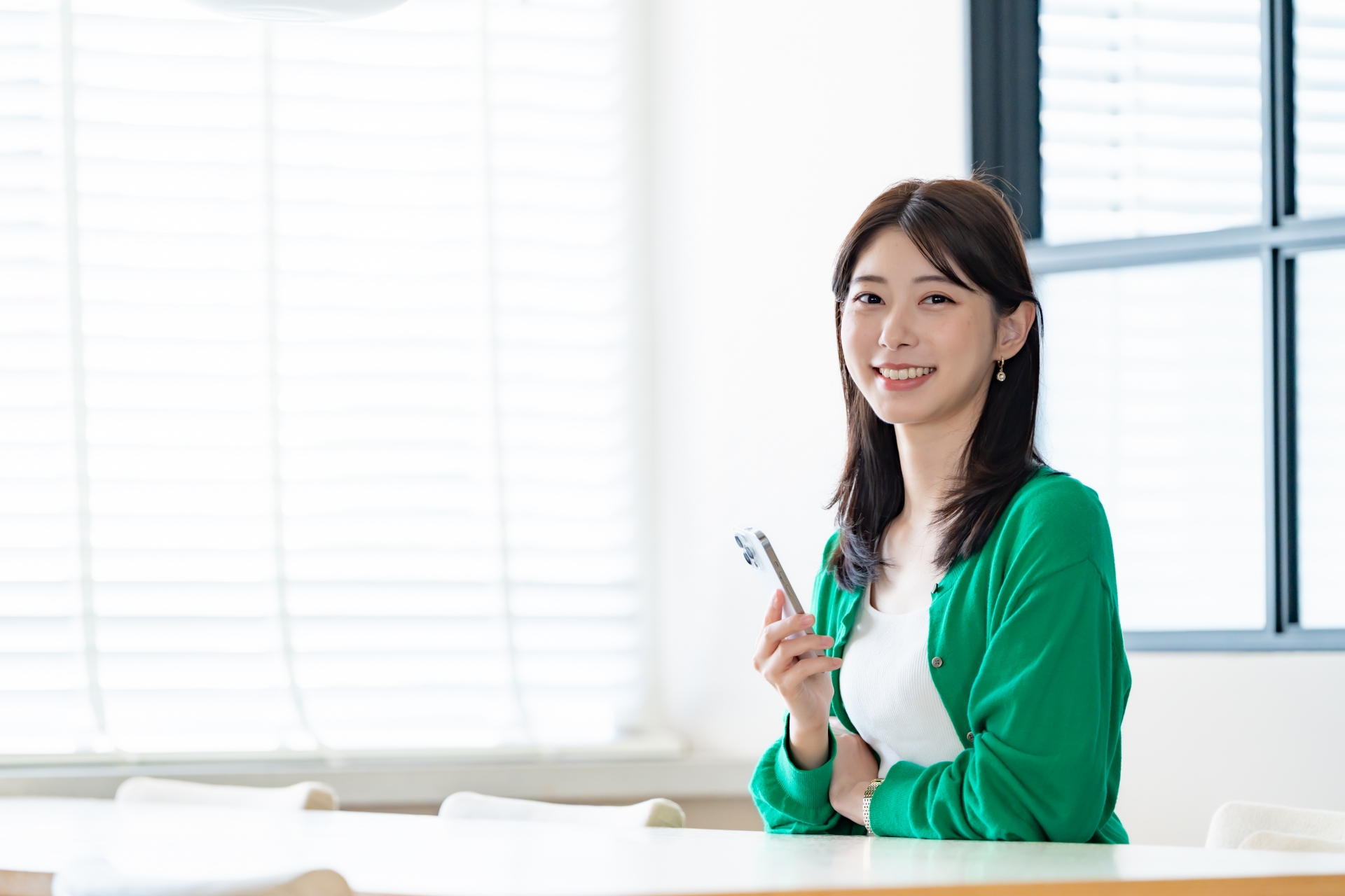 室内でスマートフォンを持ち微笑む女性