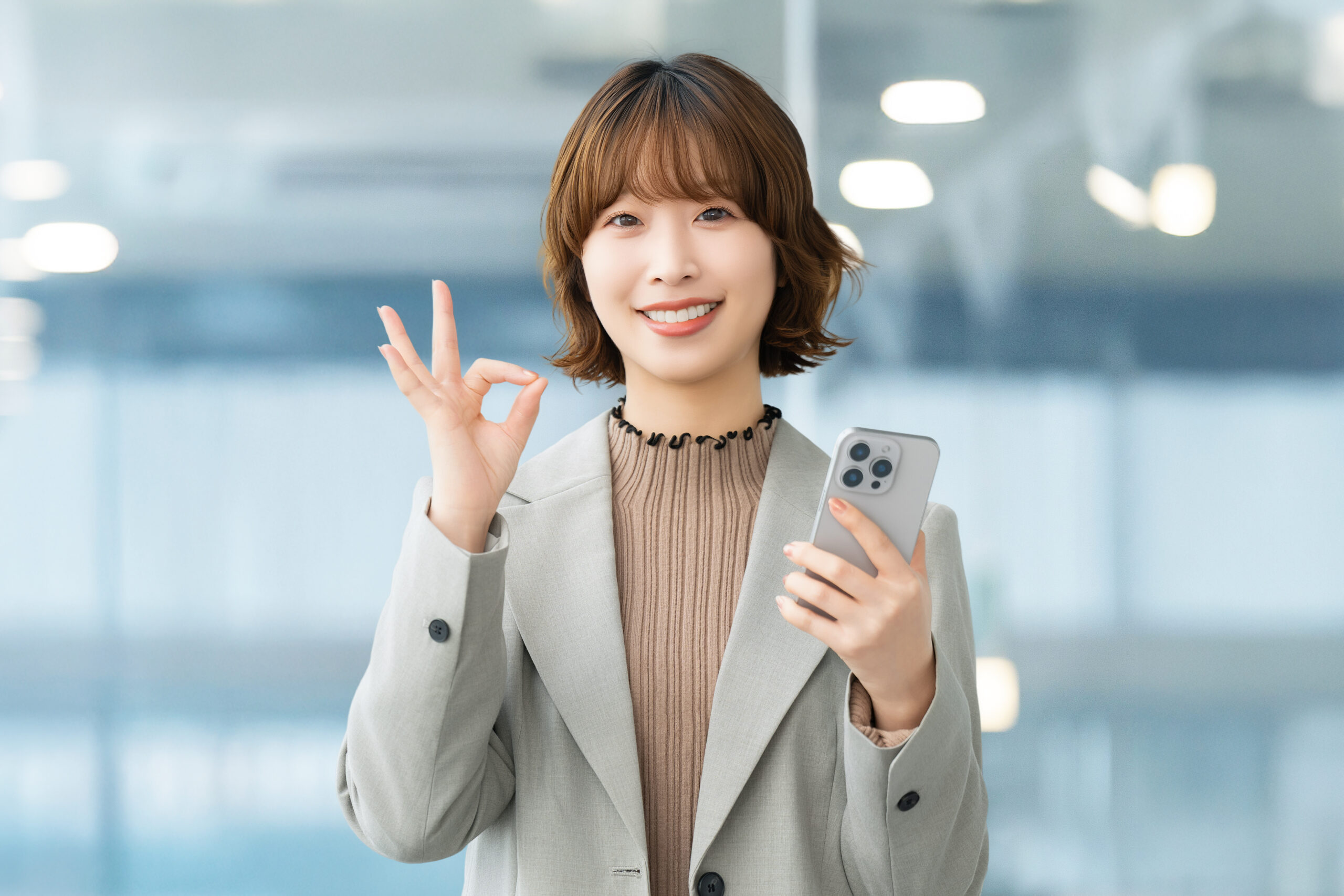 スマホを持ってOKポーズをする笑顔の女性