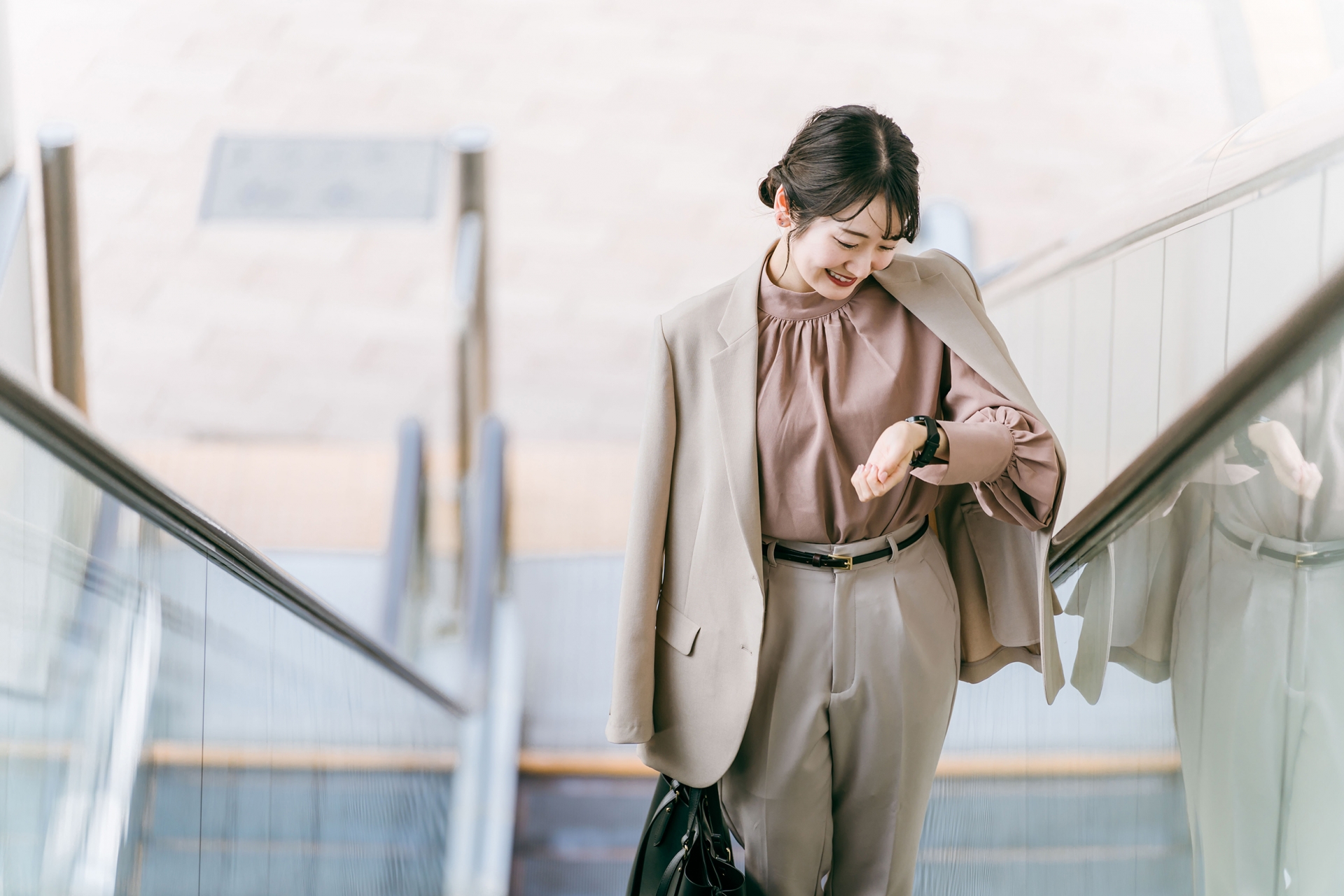 駅のエスカレーターで腕時計を見る女性