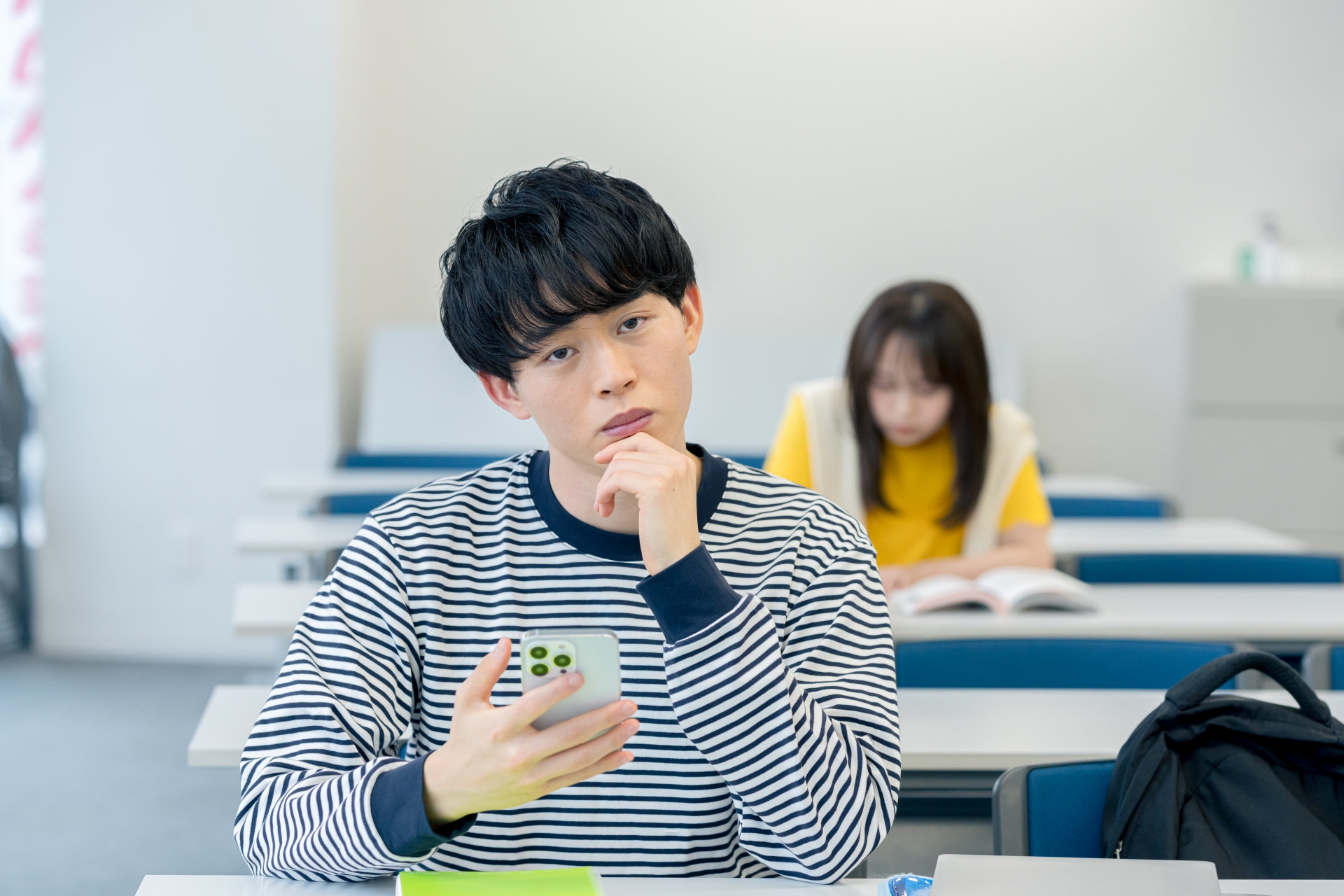 スマホを見ながら悩む大学生
