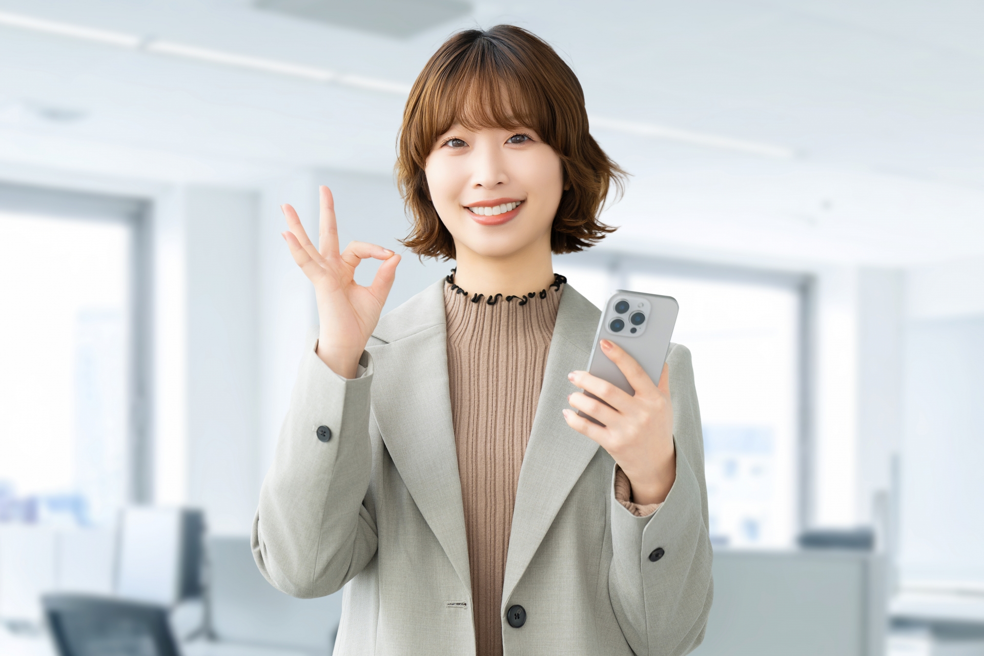 スマホを持ってOKポーズをする笑顔の女性