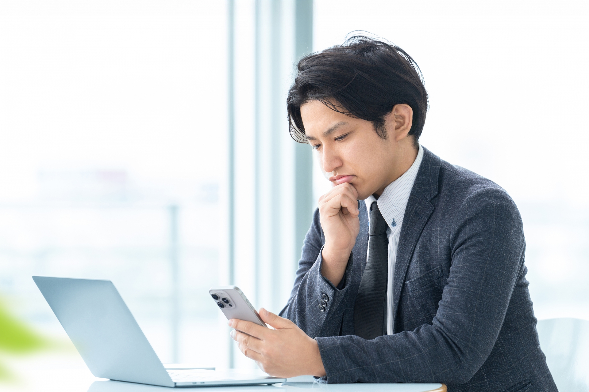 パソコンの前でスマホを見ながら考える男性