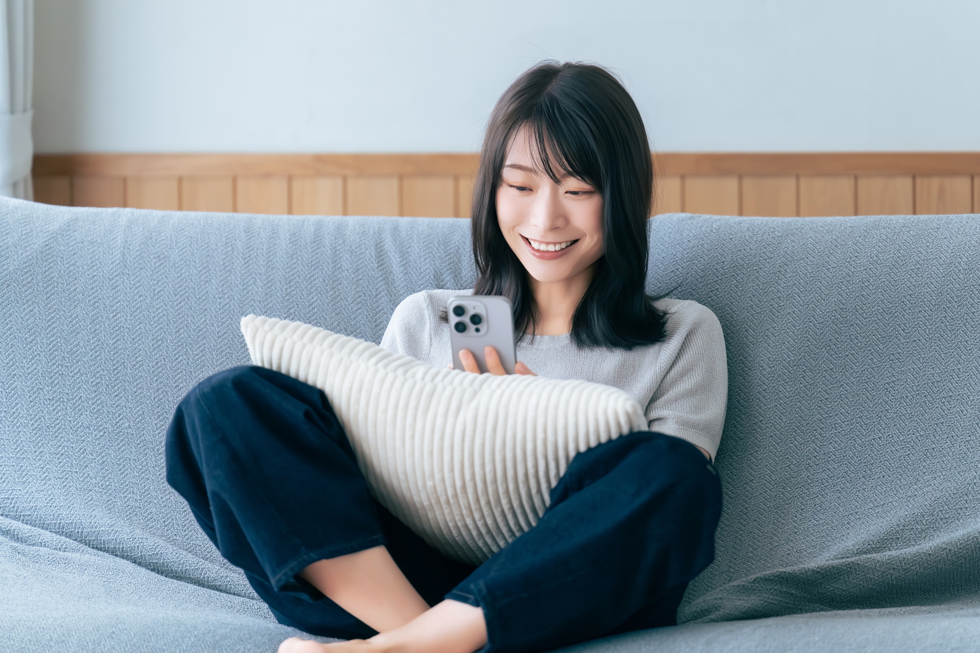 ソファに座ってスマホを使う笑顔の女性