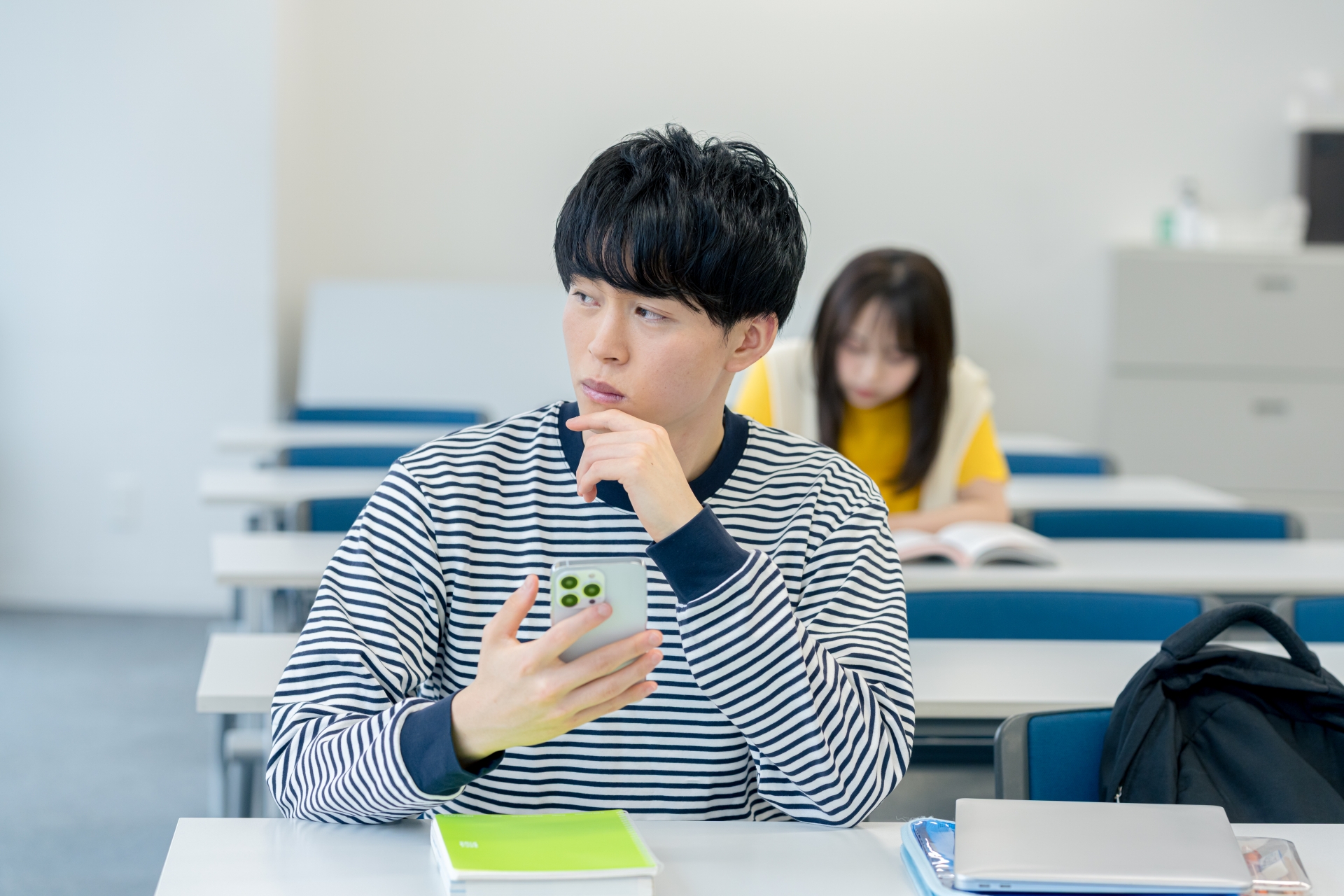 スマホを見ながら悩む大学生