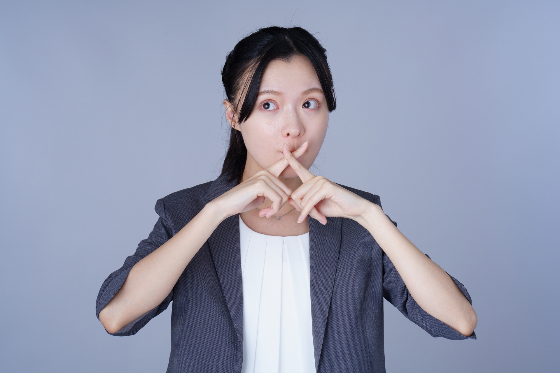 口元でバツ印を作るスーツを着た女性