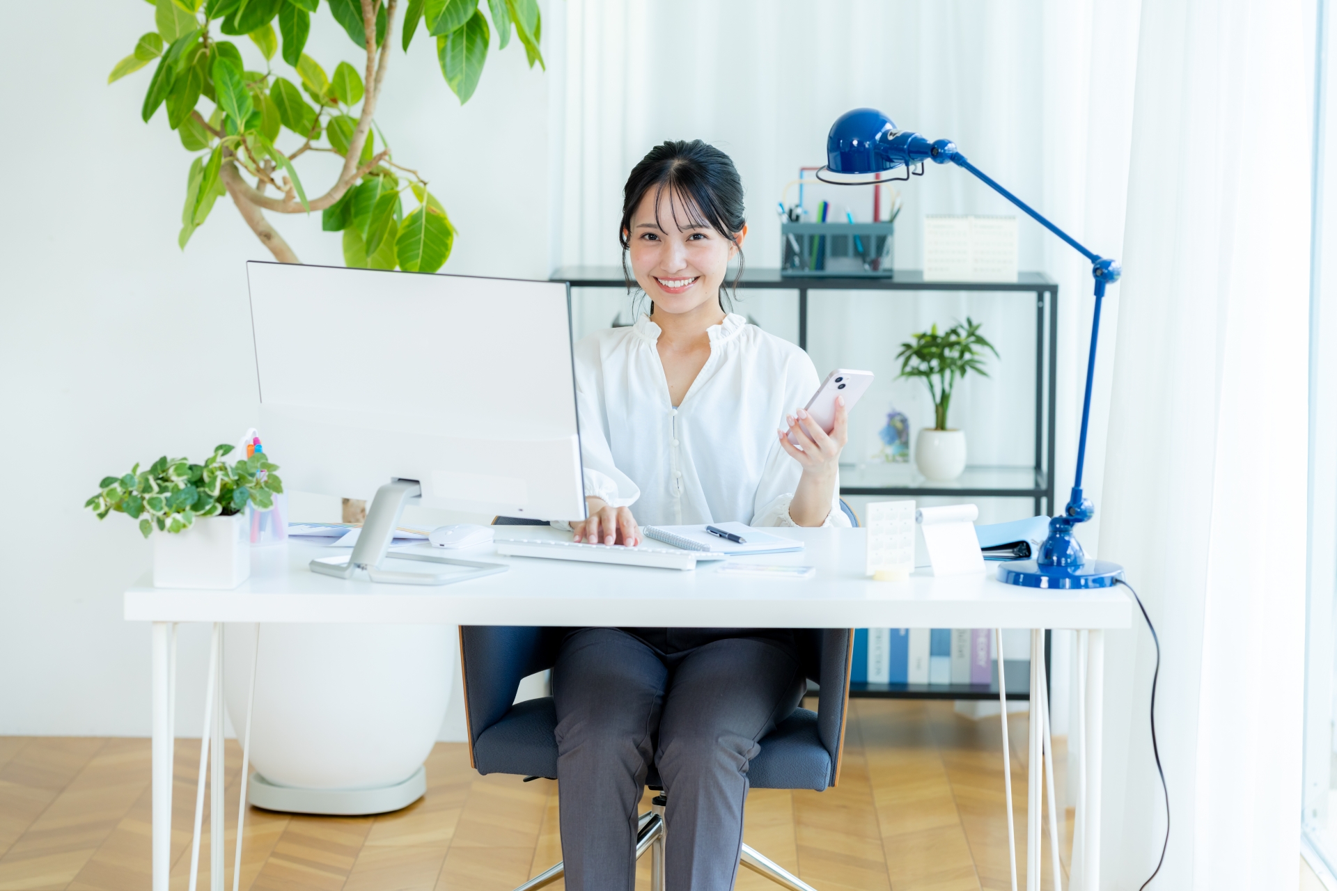 デスクトップPCの前でスマホを持つ笑顔の女性