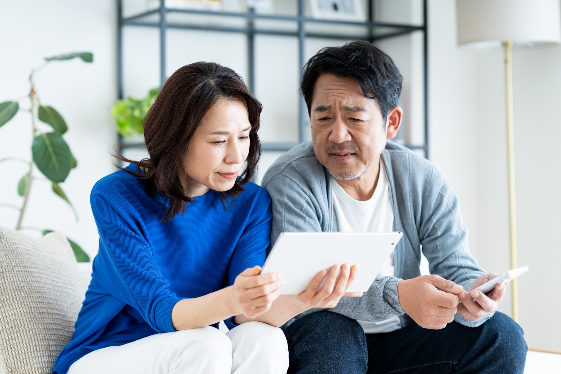 リビングでタブレットを見るミドルの夫婦