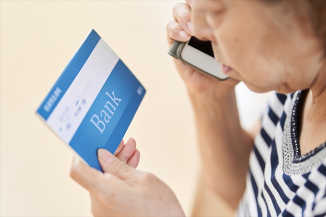 通帳を見て電話をかける女性