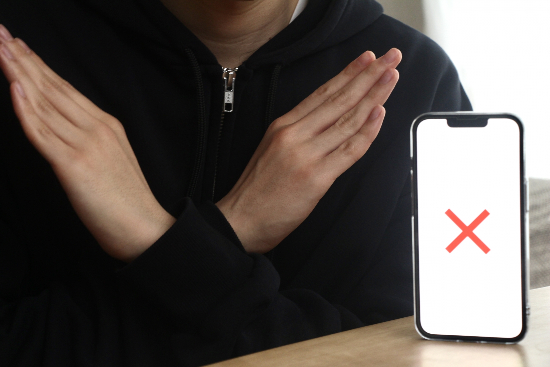 スマホとバツポーズの男性の手