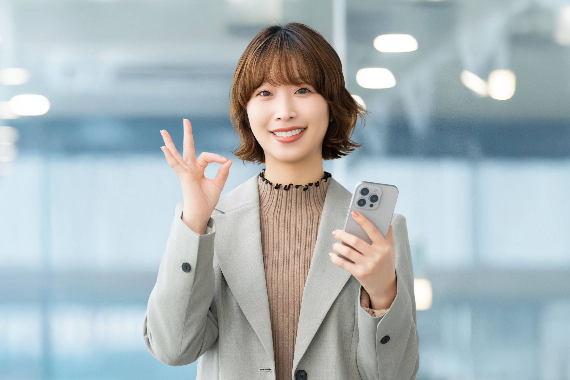 スマホを持ってOKポーズをする笑顔の女性