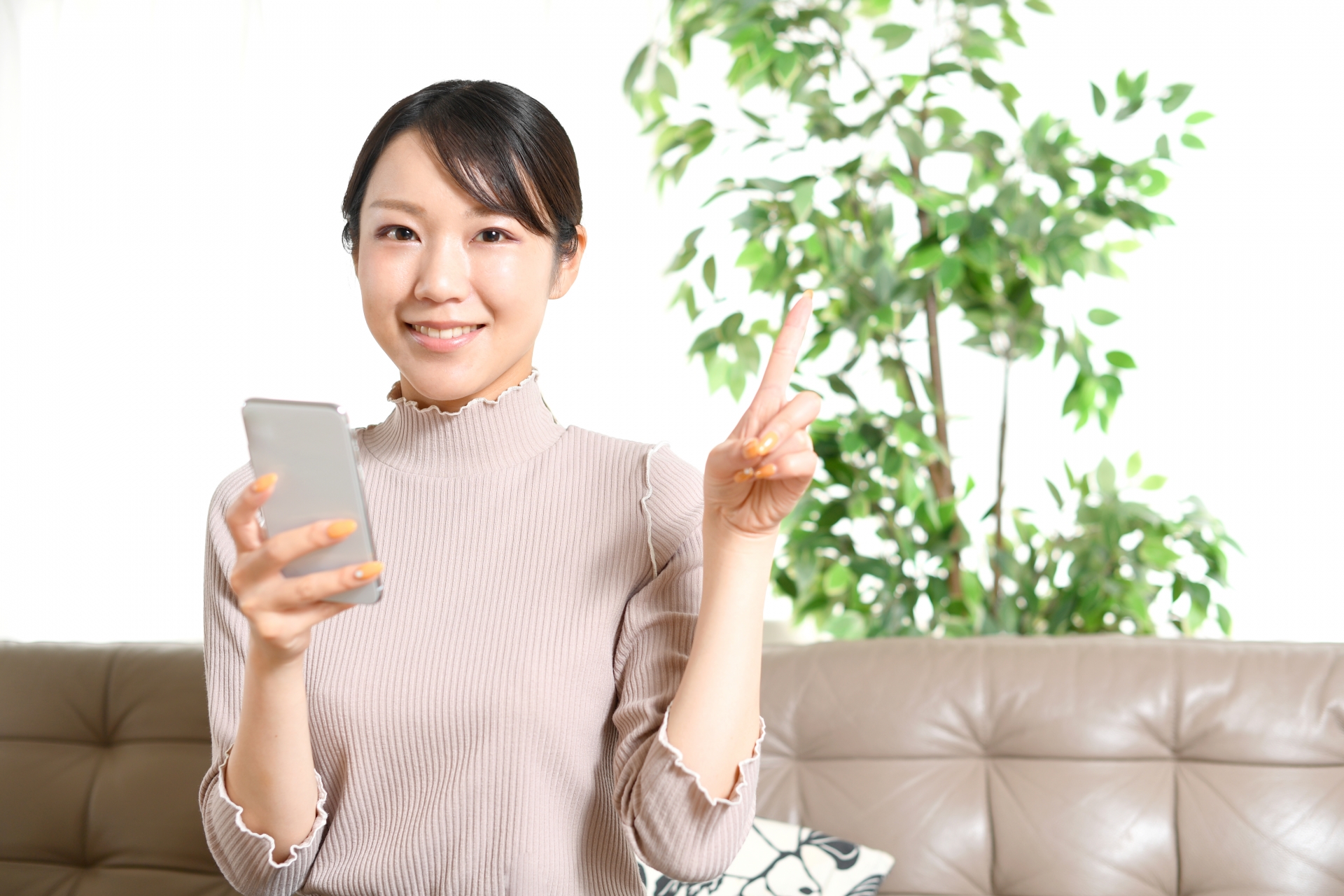 スマホを持ちながら人差し指を立てる若い女性