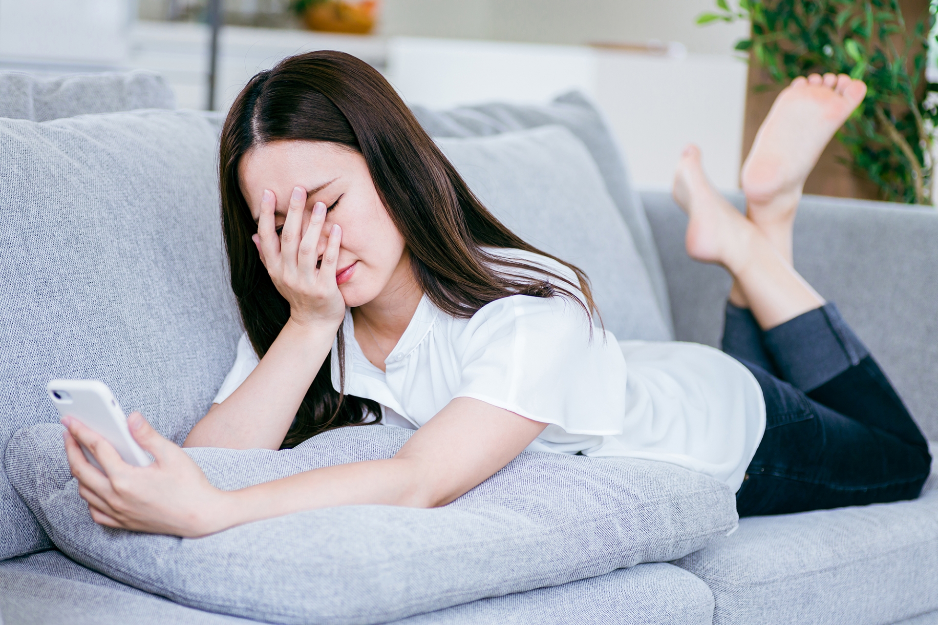 ソファで寝転んでスマホを使う女性