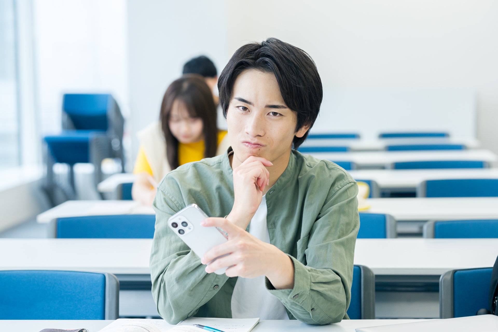 スマホを見ながら悩む大学生