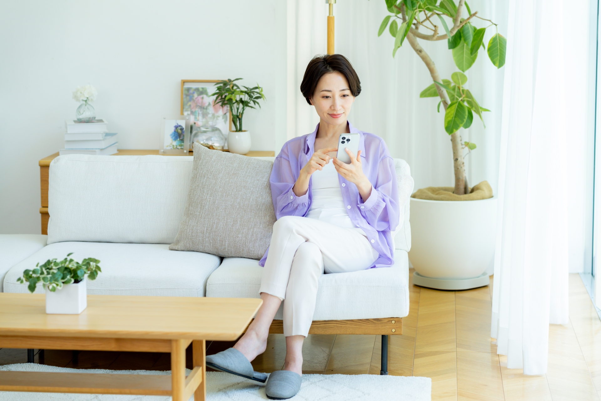 ソファで足を組んでスマホを操作する女性