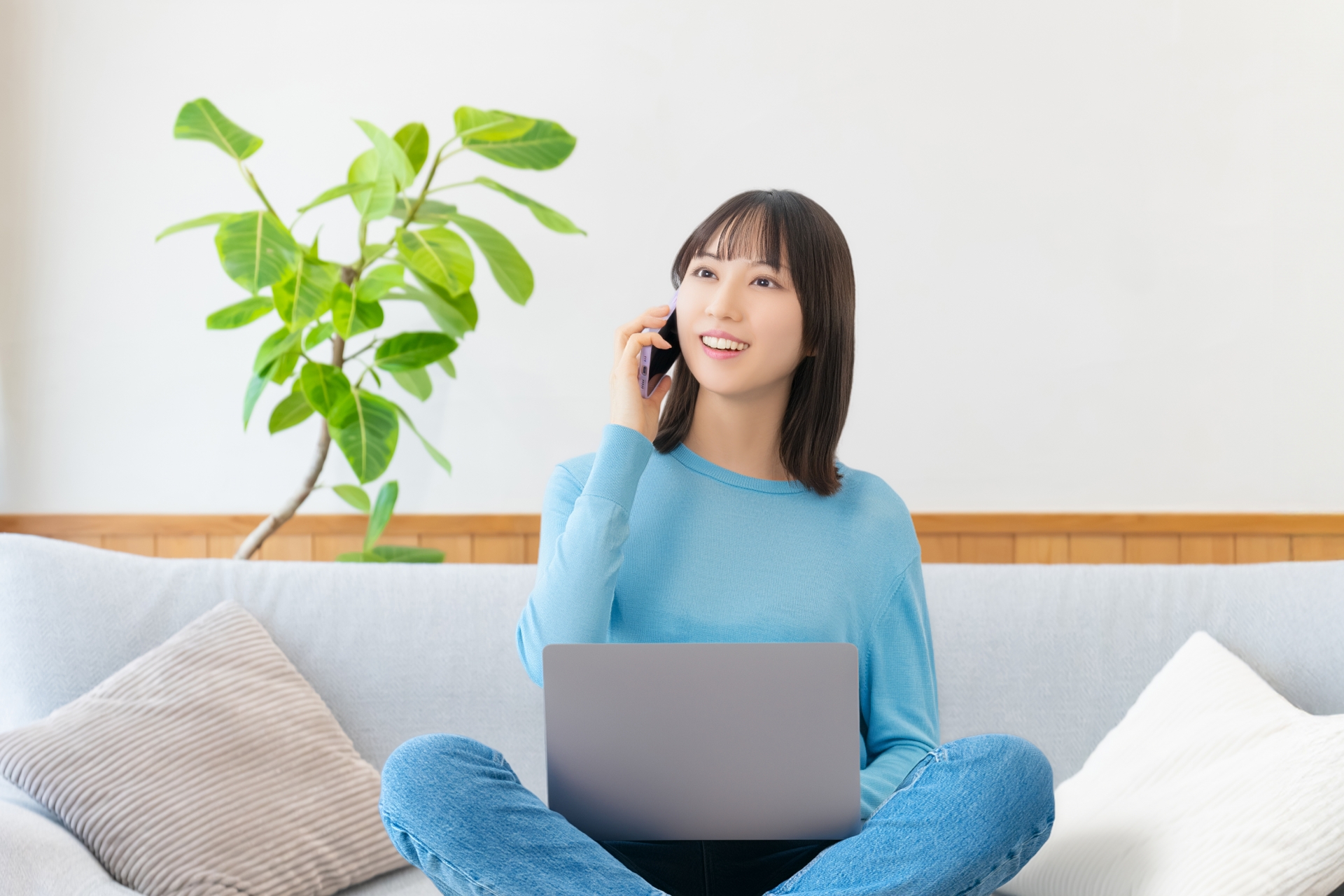 ソファに座ってスマホとパソコンを使う女性