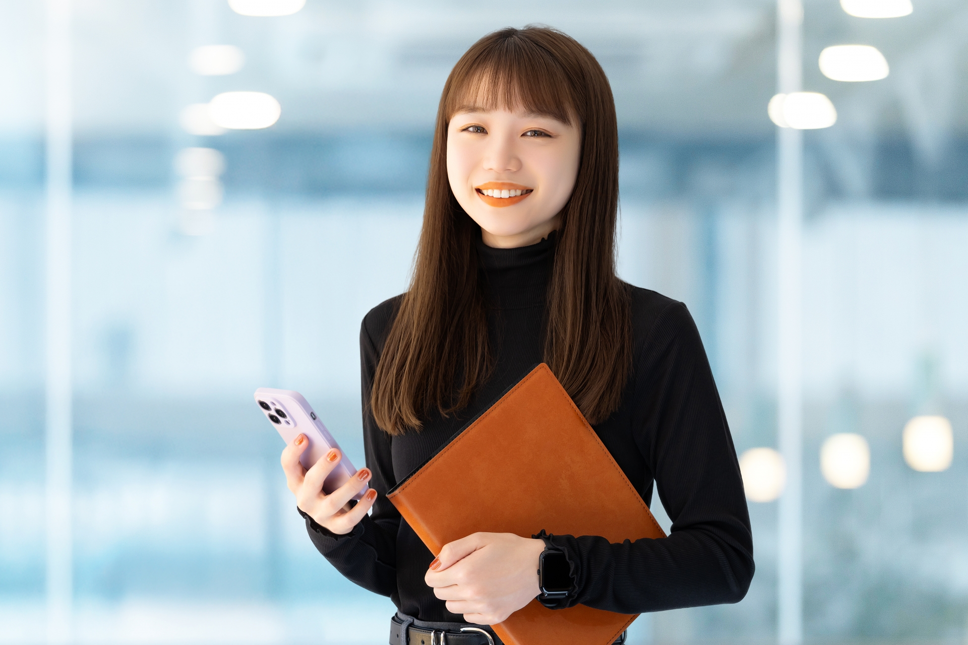 スマホとバインダーを持つ笑顔の女性