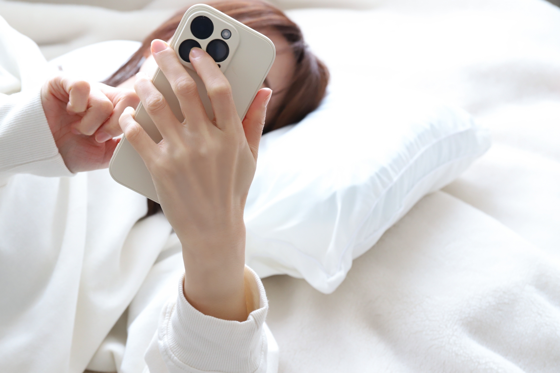 ベッドでスマートフォンを見る女性