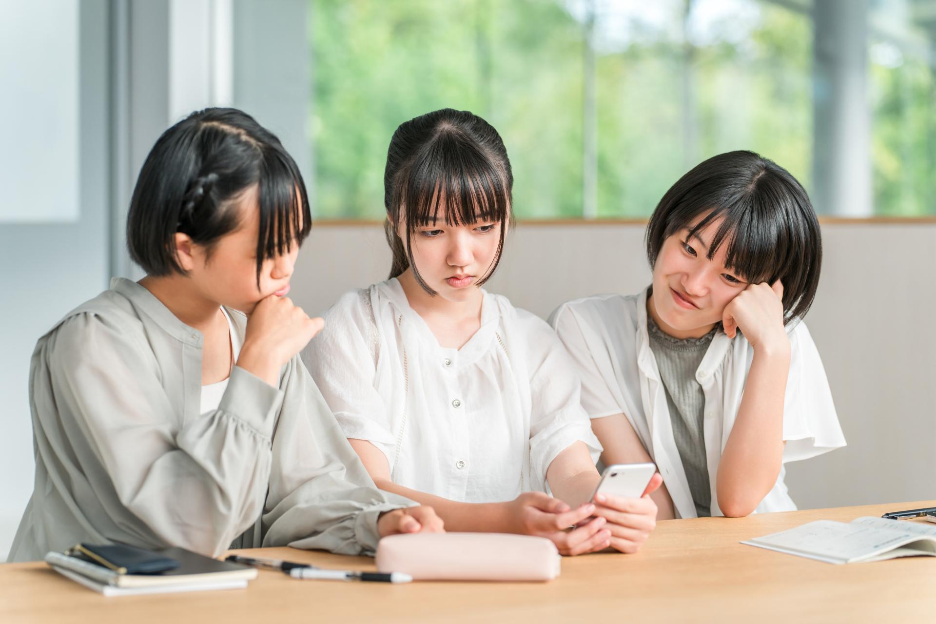 テーブルでスマートフォンを見ながら話す3人の女性