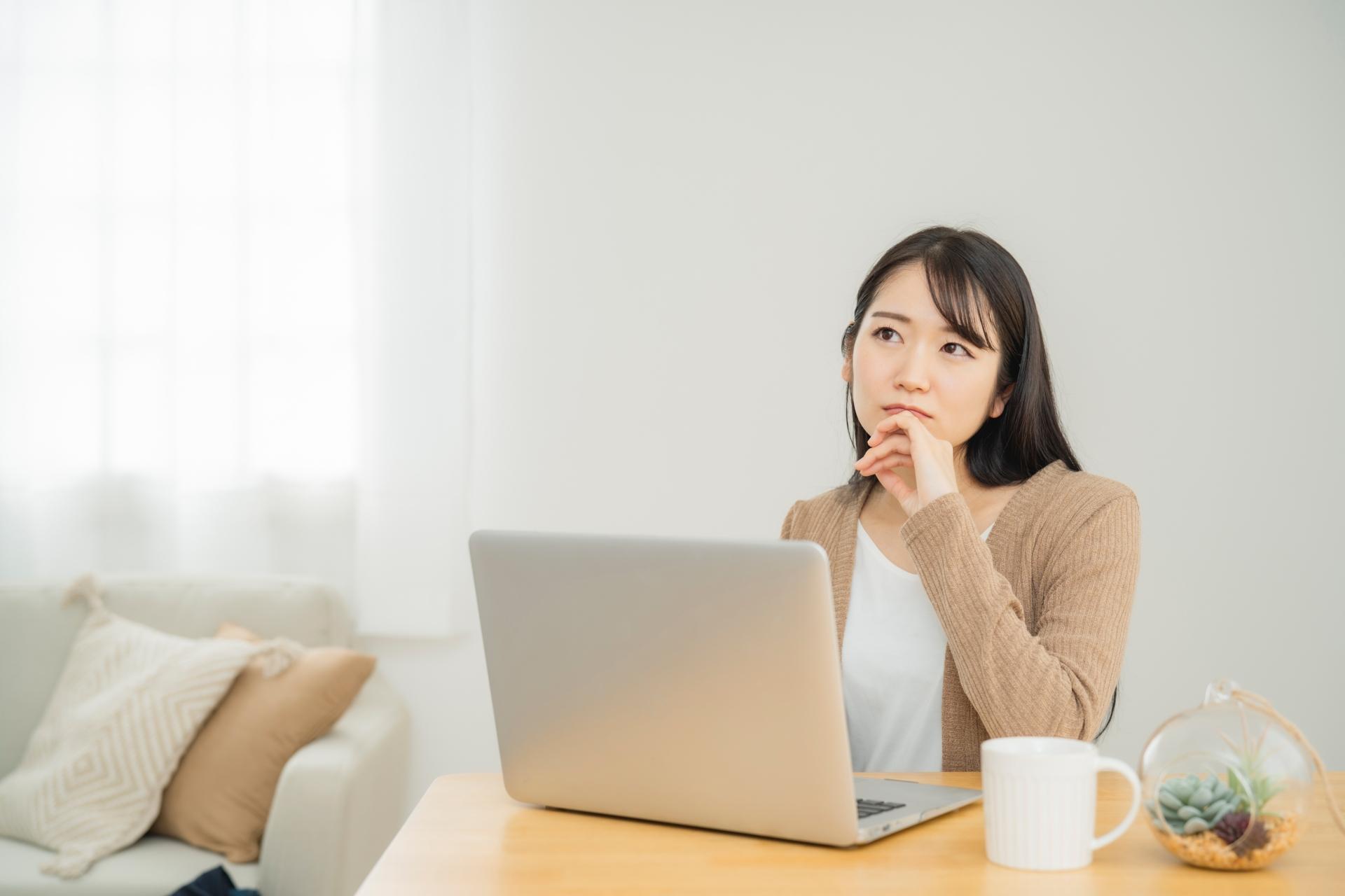 ノートパソコンの前で考える女性