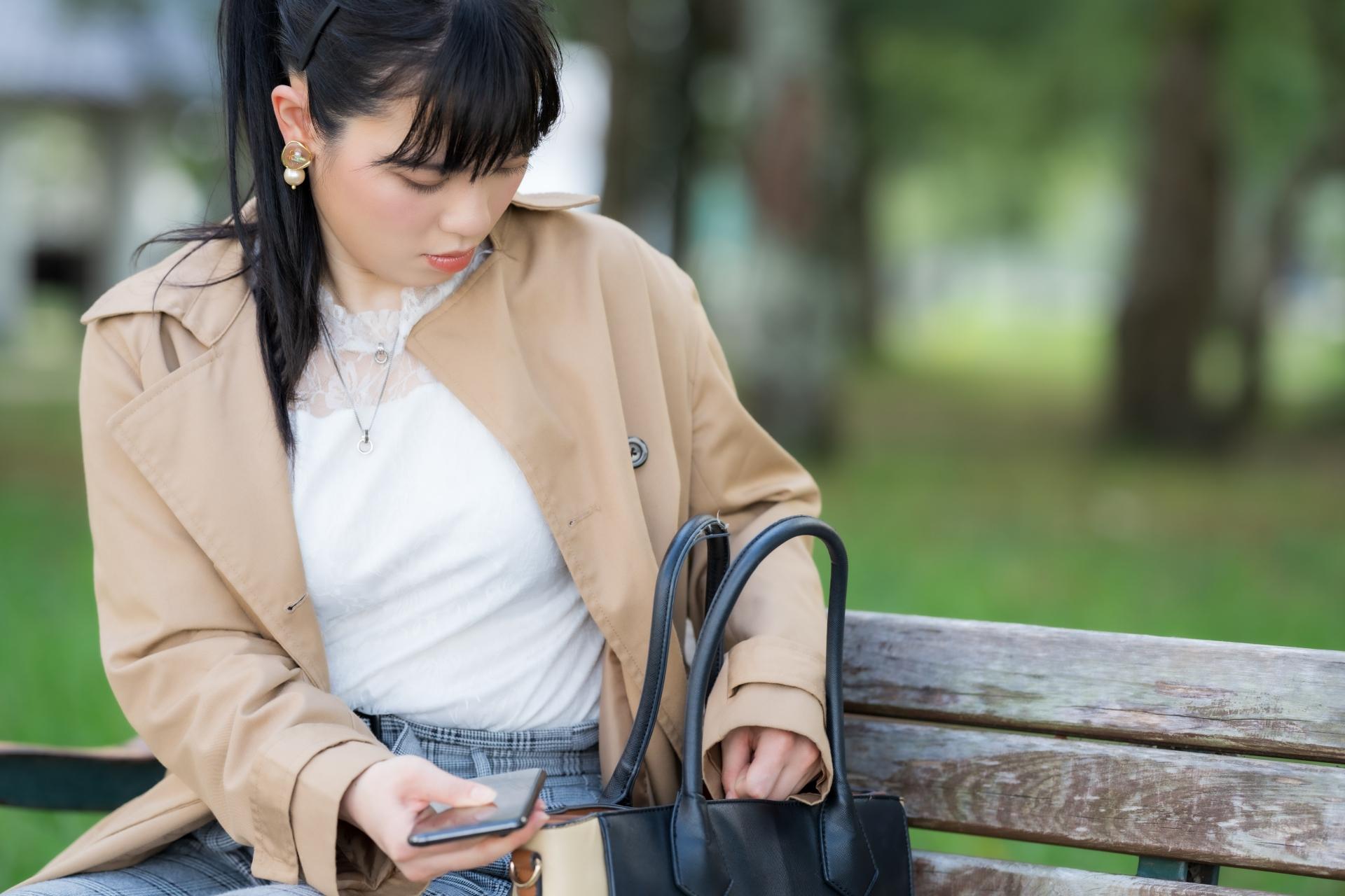 ベンチでバッグの中を探す女性
