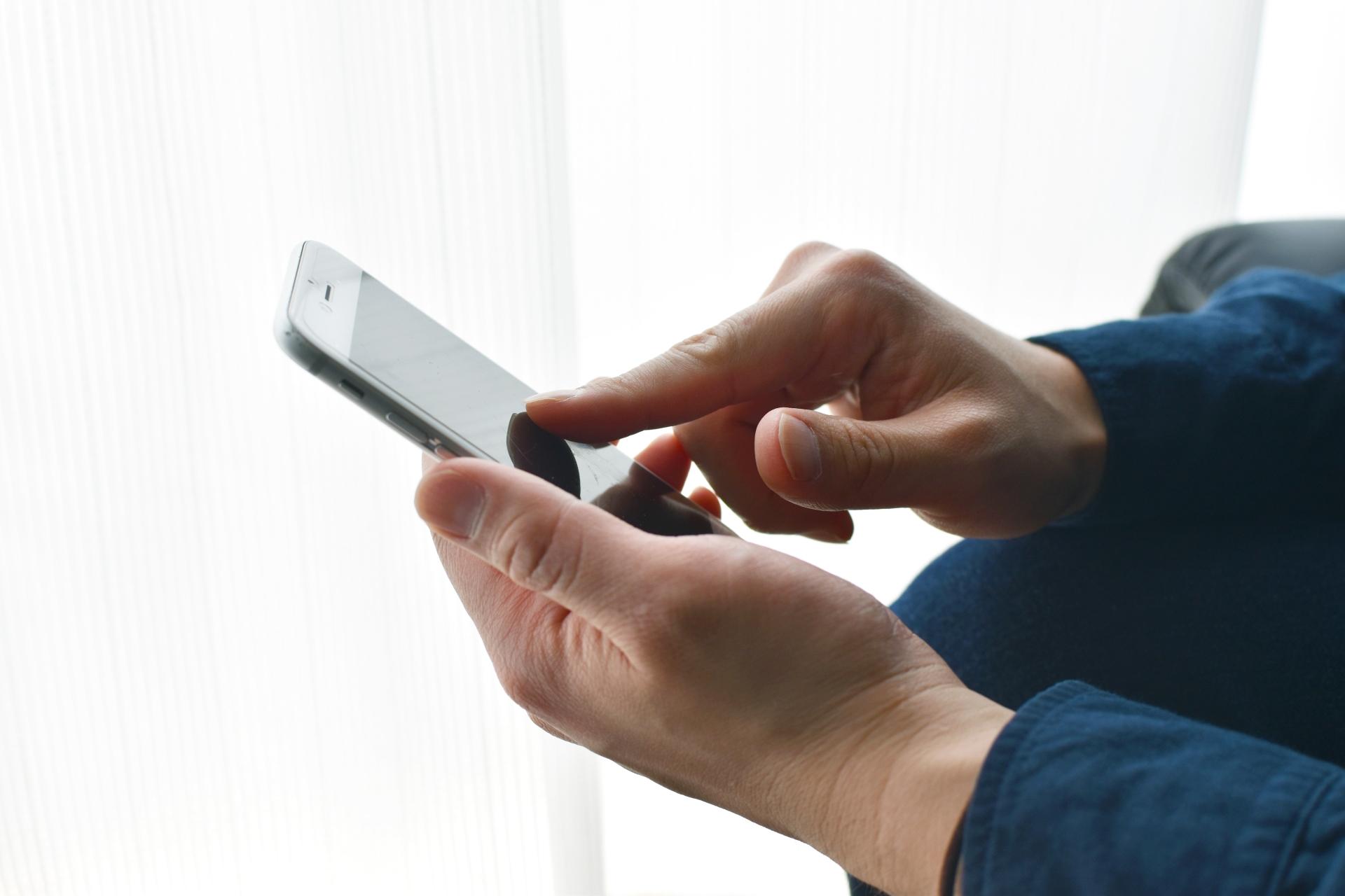 窓際でスマートフォンを操作する手元