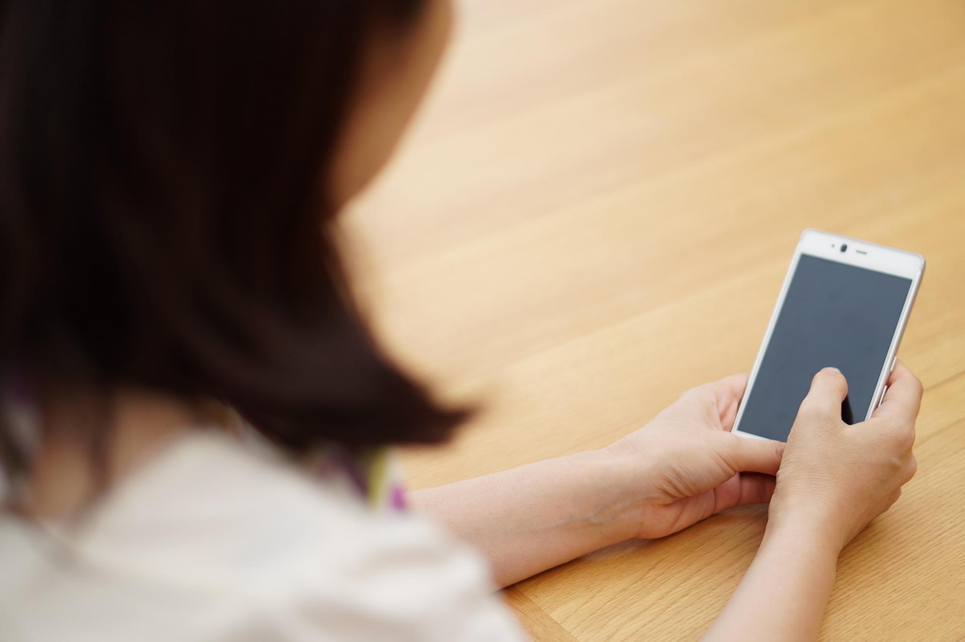 机でスマートフォンを操作する女性の手元