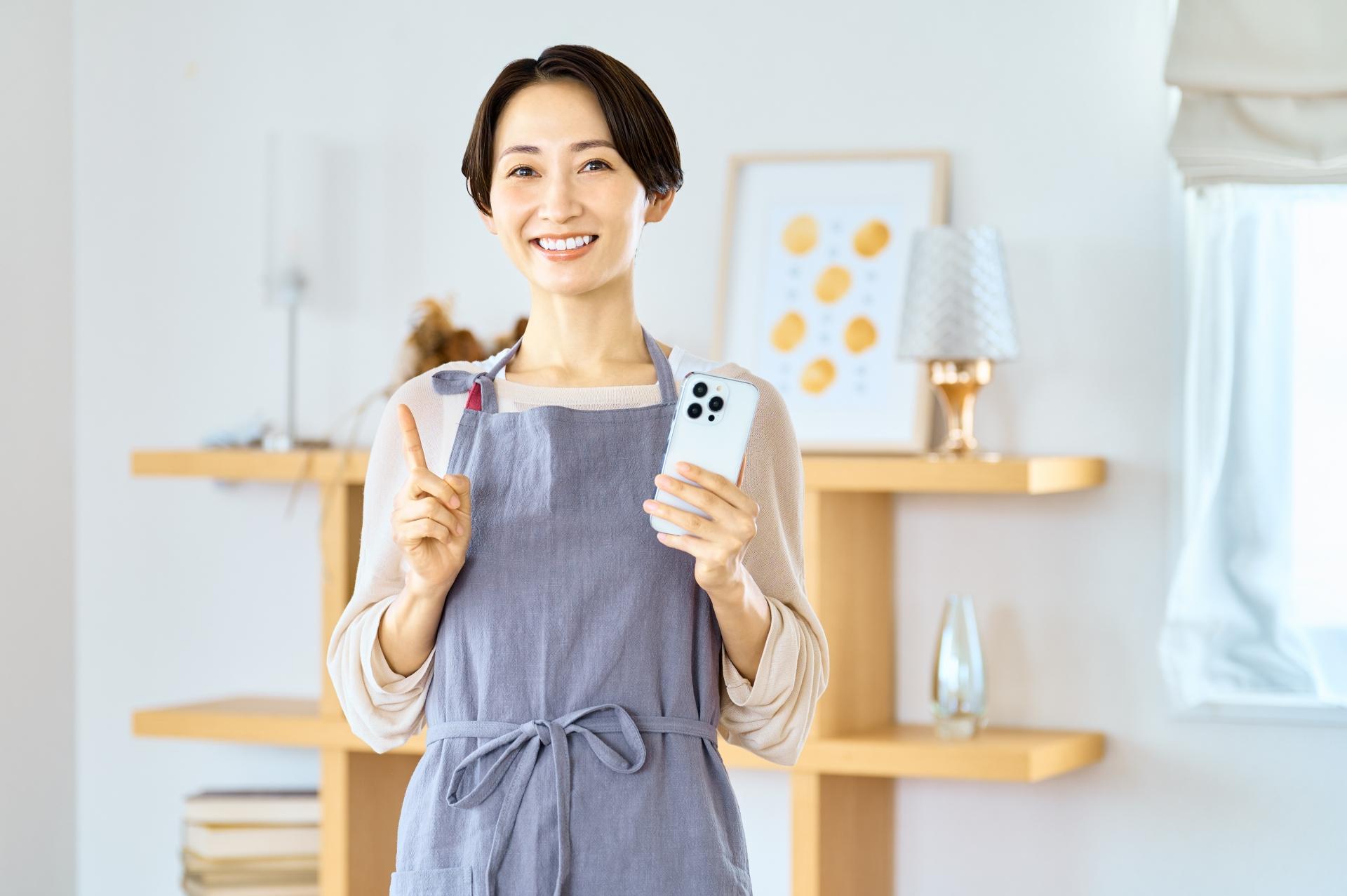 スマートフォンを持って案内するエプロン姿の女性