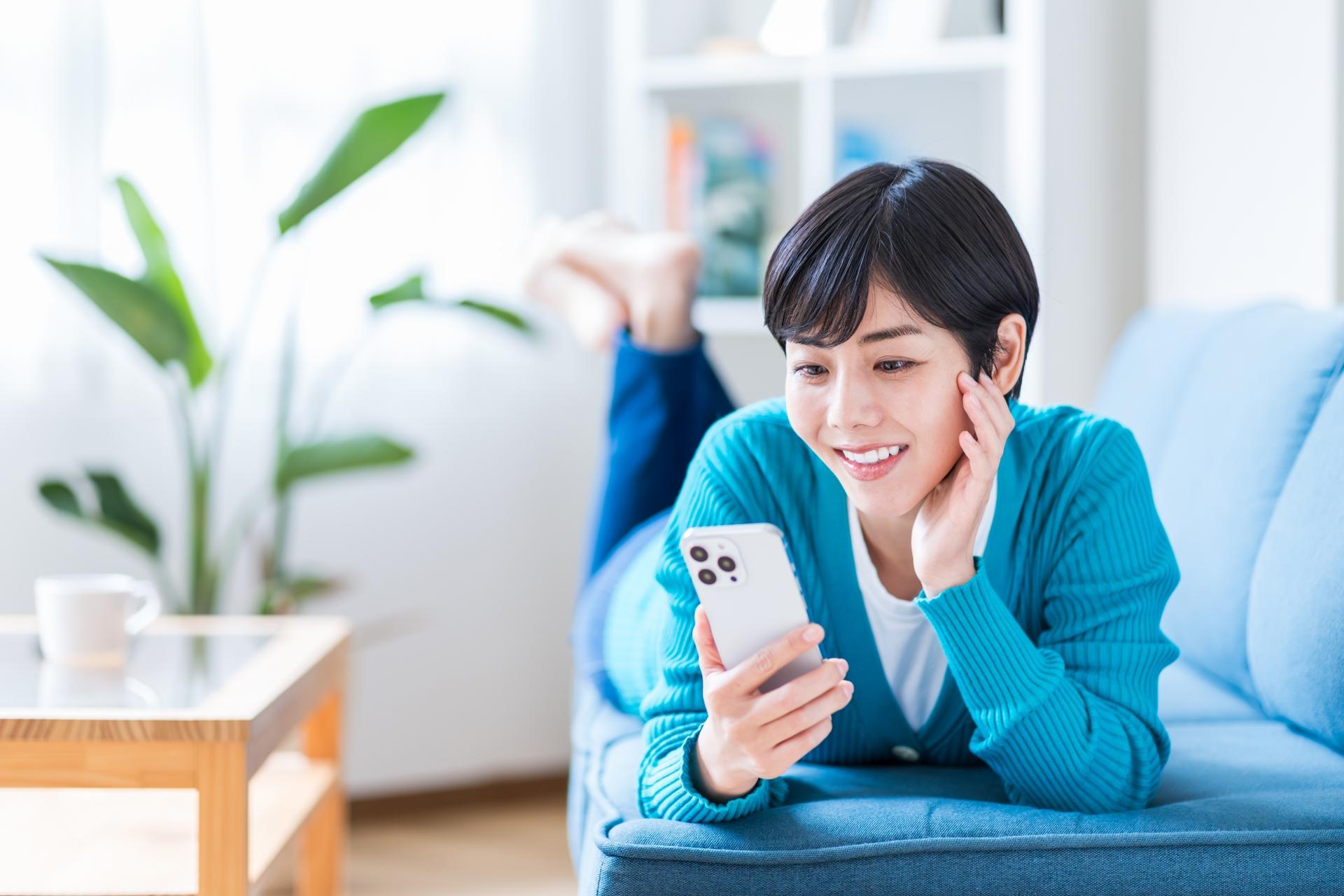 ソファでくつろぎながらスマートフォンを見る女性