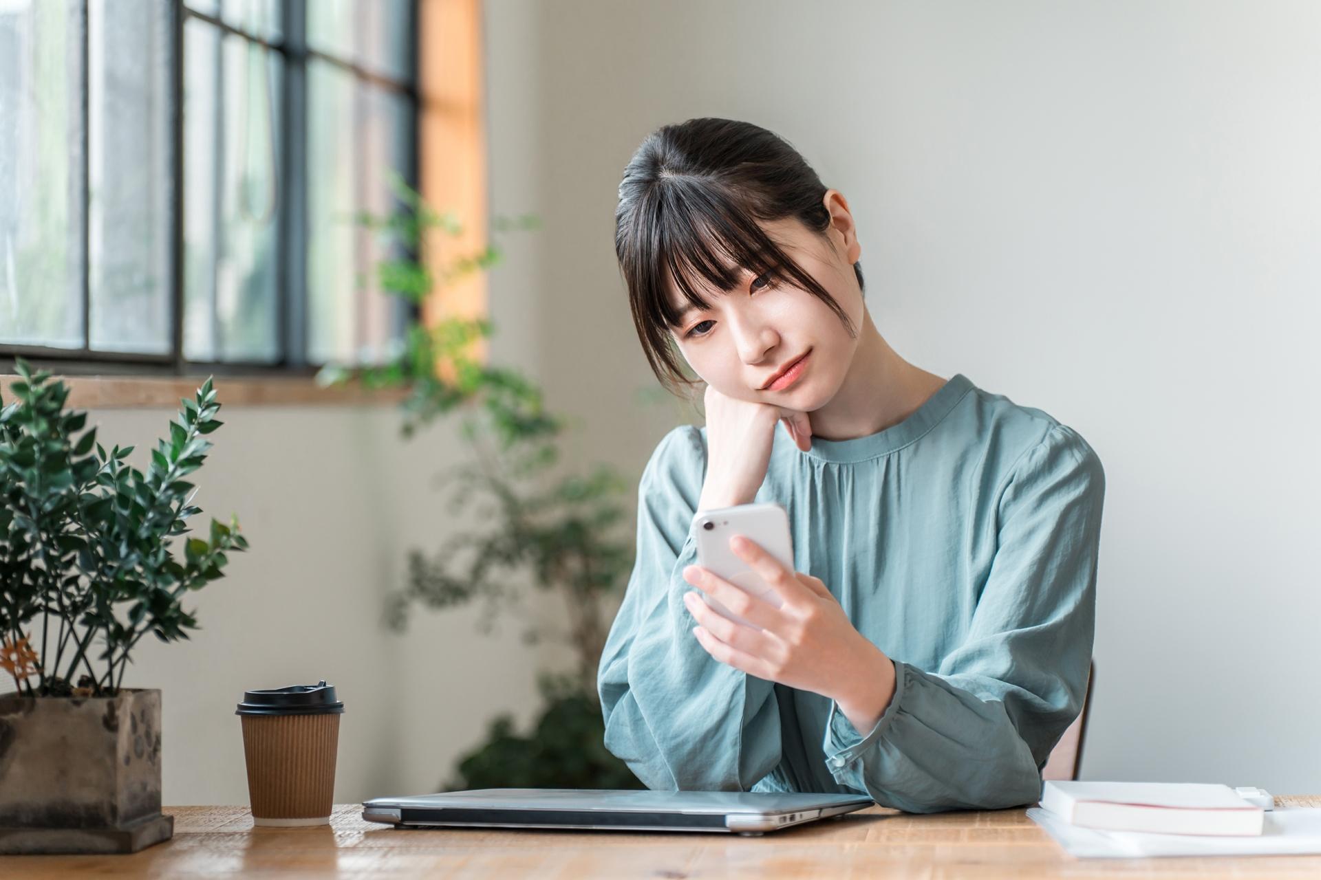 テーブルでスマートフォンを見て悩む女性