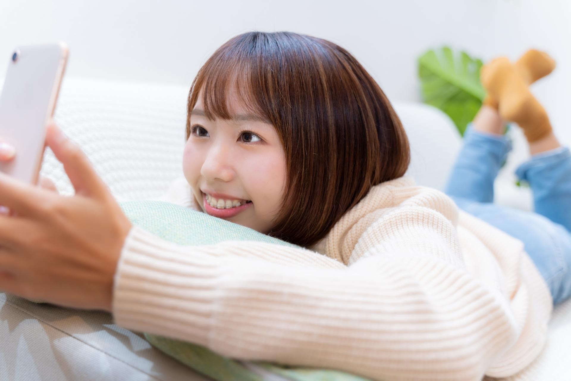 横になってスマートフォンを楽しむ女性