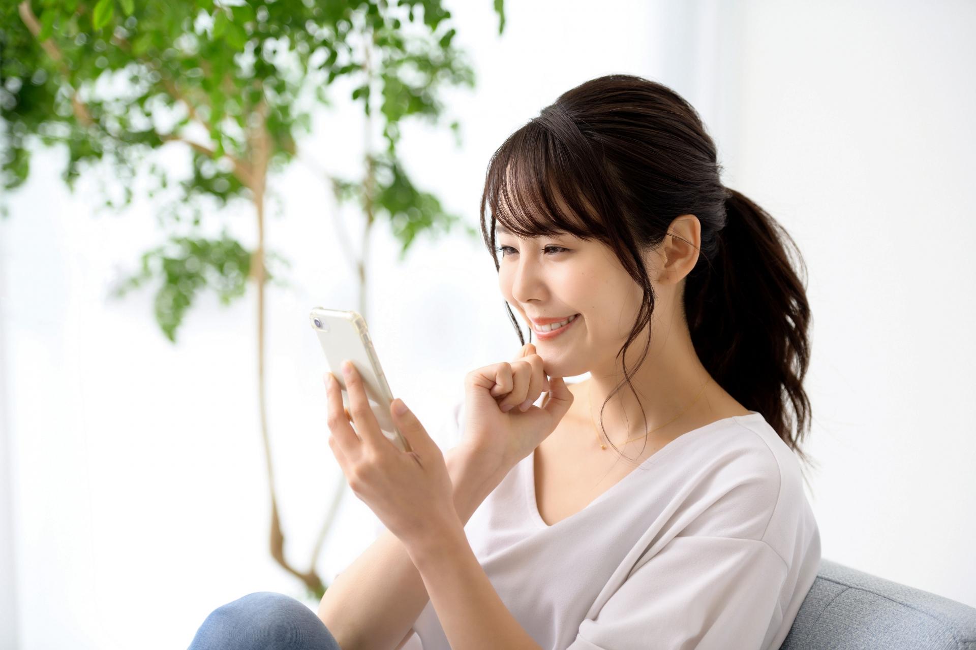 窓際でスマートフォンを見る女性