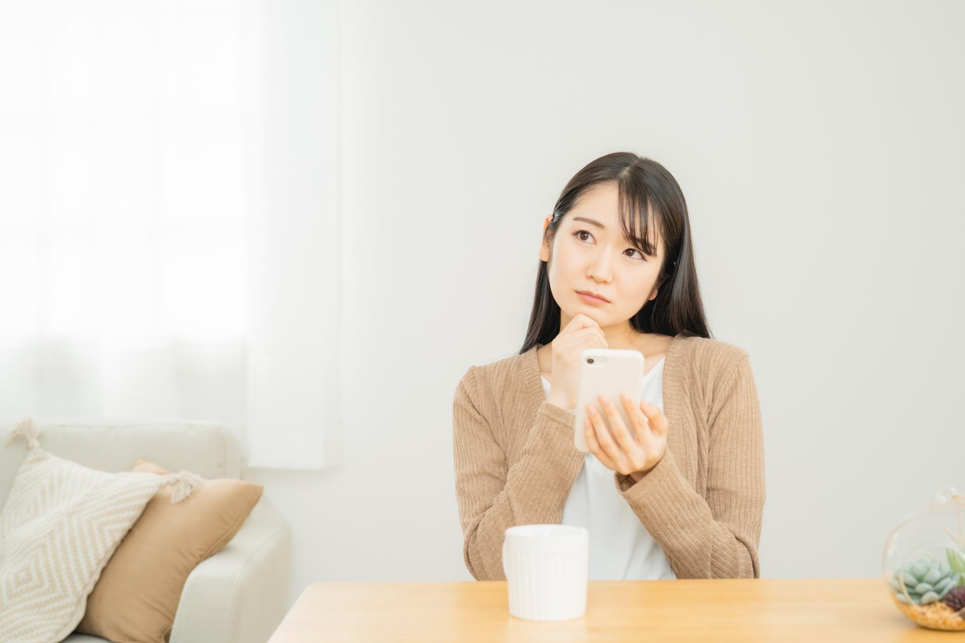スマートフォンを持って考える女性