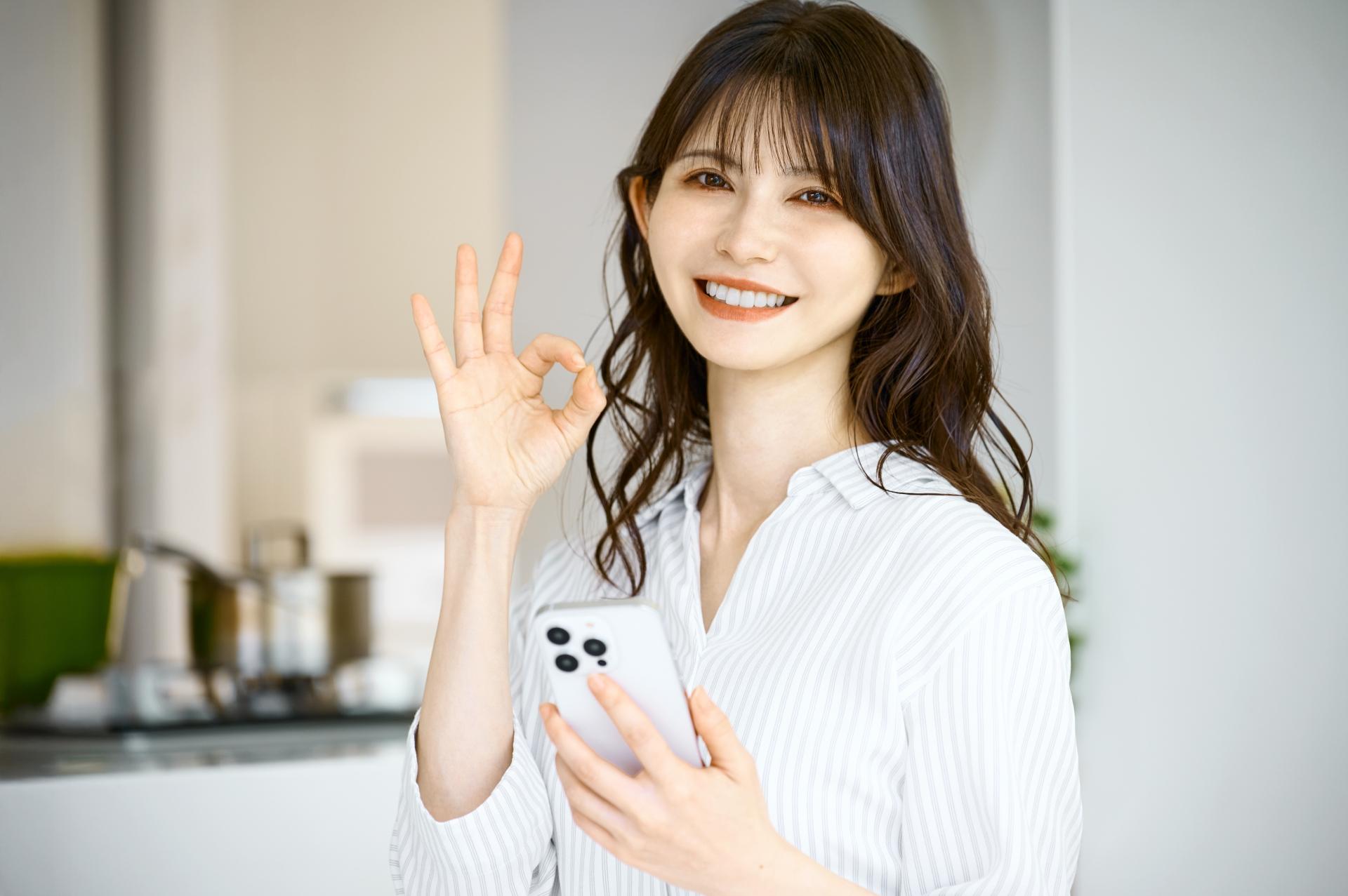 スマートフォンを持ちOKサインをする女性