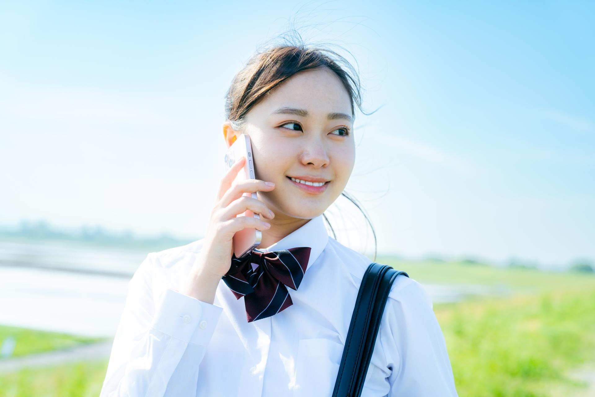 屋外でスマートフォンによる通話をする制服姿の生徒