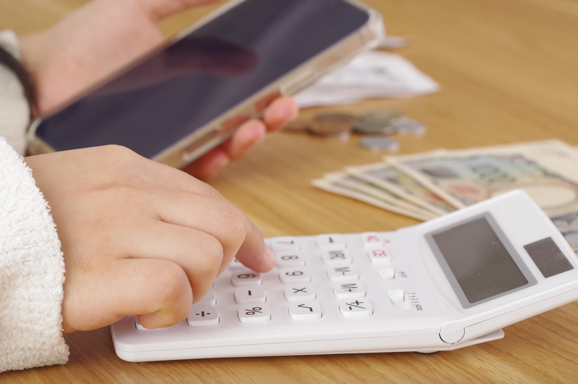 スマートフォンの横で電卓を操作する手元