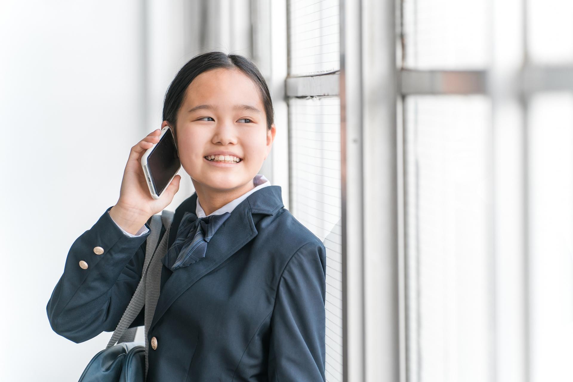 窓際でスマートフォンによる通話をする制服姿の生徒