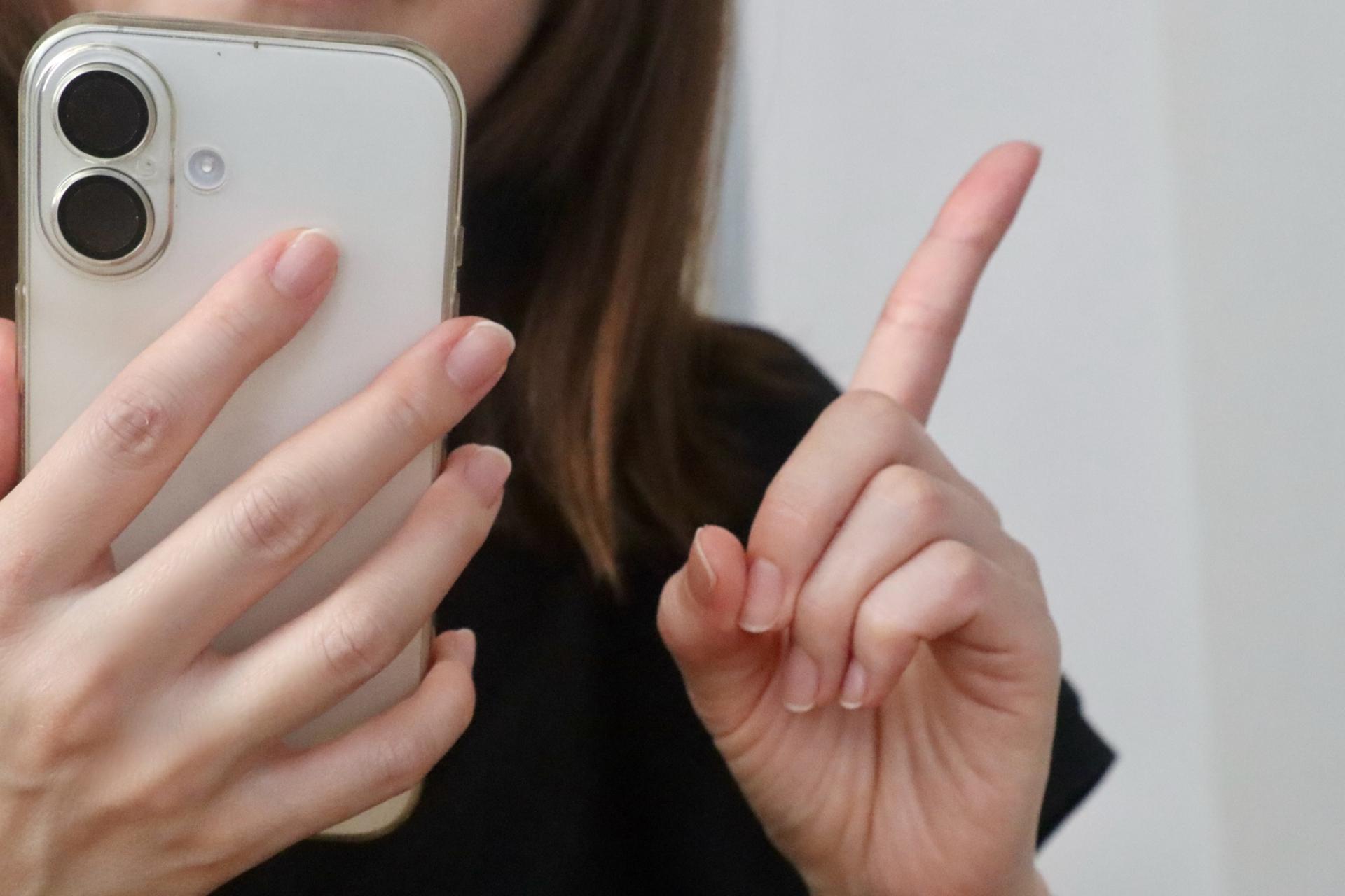 スマートフォンを持ち指を立てて説明する手元