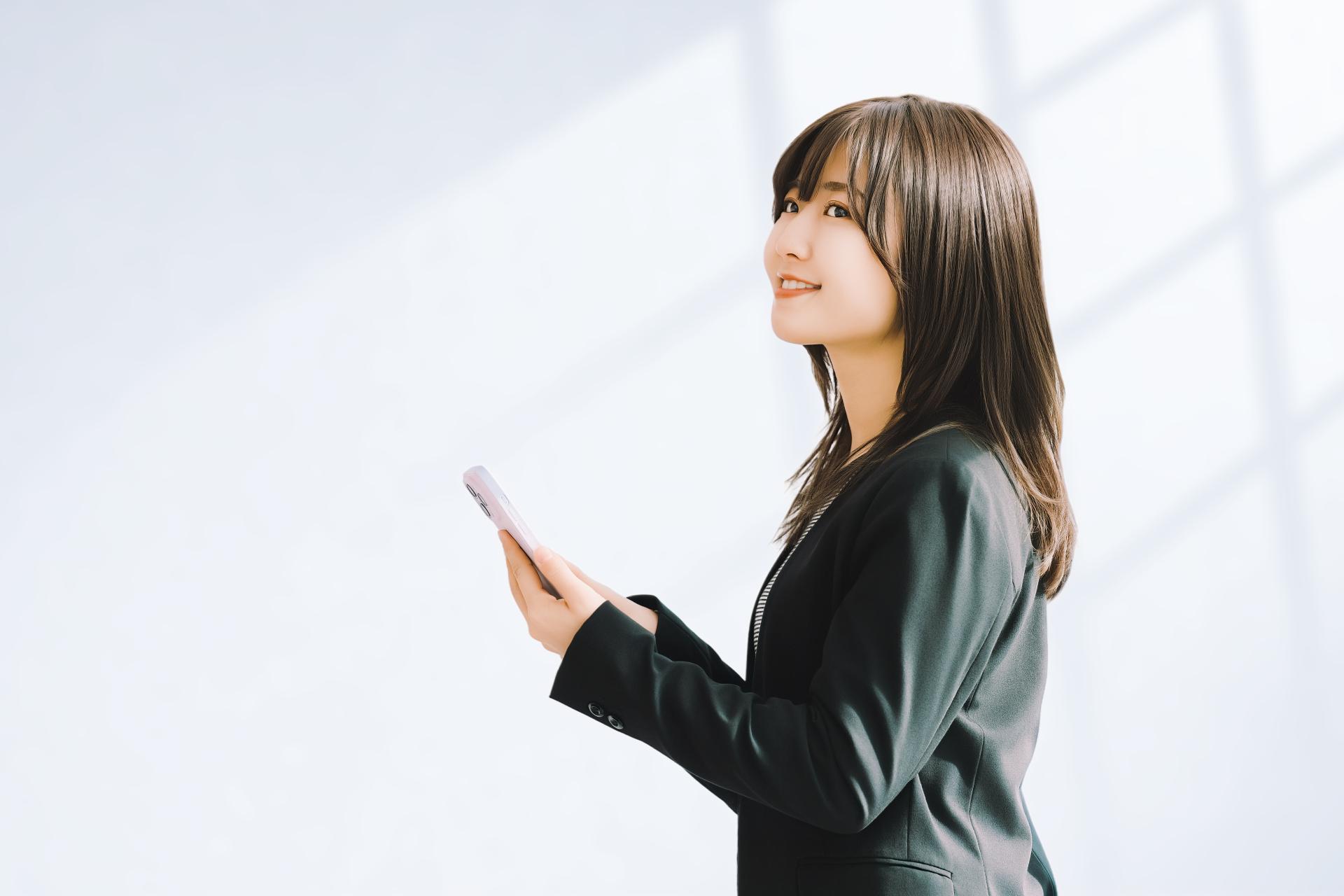 スマートフォンを手に考えるスーツ姿の女性