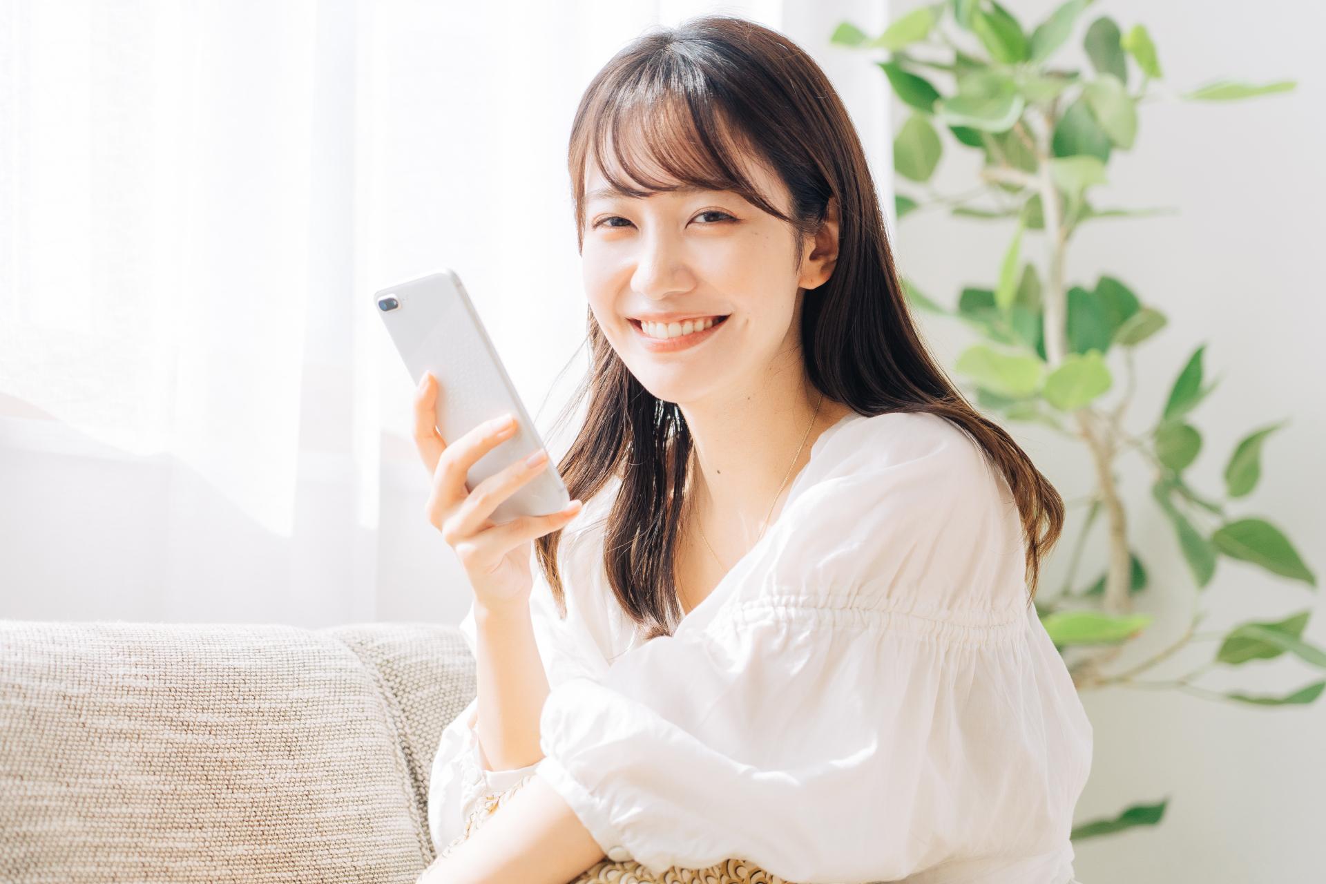 ソファでスマートフォンを持って微笑む女性